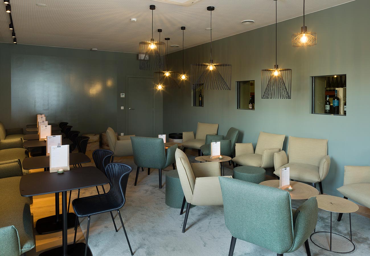 lounge met groene en beige stoelen, moderne hanglampen, een verfijnde sfeer en groene muren door In't Kleur.