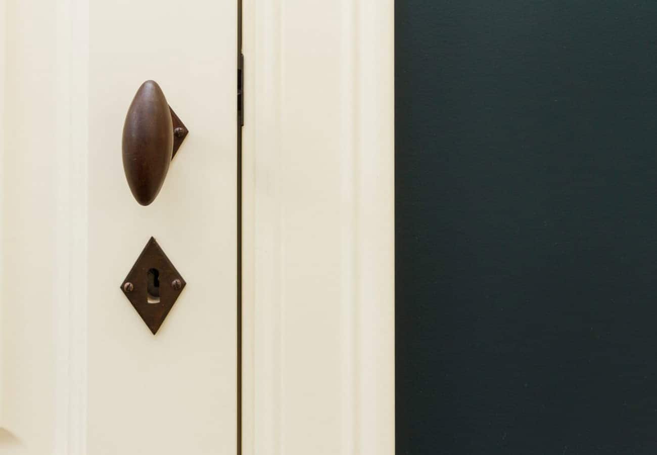 Detail van een deur met een klassieke, donkerbruine deurknop naast een donkergroene muur door In't Kleur.