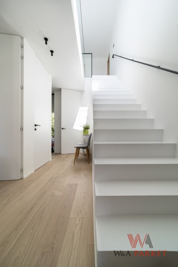 Witte trap en witte muren door In't Kleur in modern interieur met houten parketvloer en strakke lijnen.