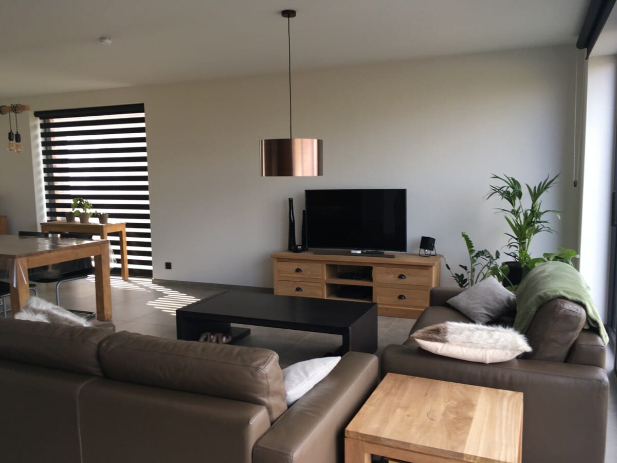 Woonkamer met leren zetels, houten meubels, planten en witte muren door In't Kleur bij een project in Lebbeke.