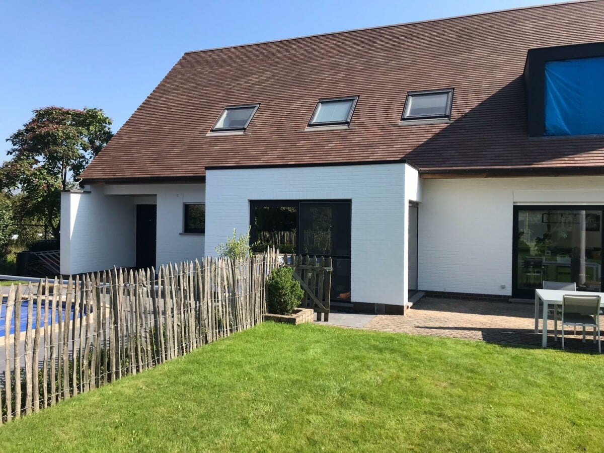 Tuin met houten omheining en een huis met witte bakstenen in Merelbeke.