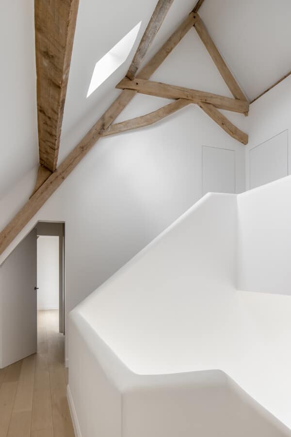 Open ruimte onder het dak met houten balken en strakke witte afwerking, project in Rollegem door In't Kleur.