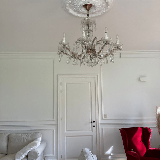 Kristallen kroonluchter in een woonkamer met witte muren en een rode fauteuil bij een project in Zottegem.