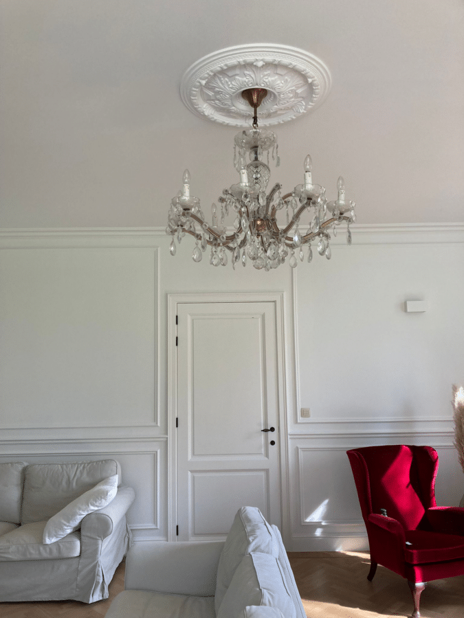 Kristallen kroonluchter in een woonkamer met witte muren en een rode fauteuil bij een project in Zottegem.