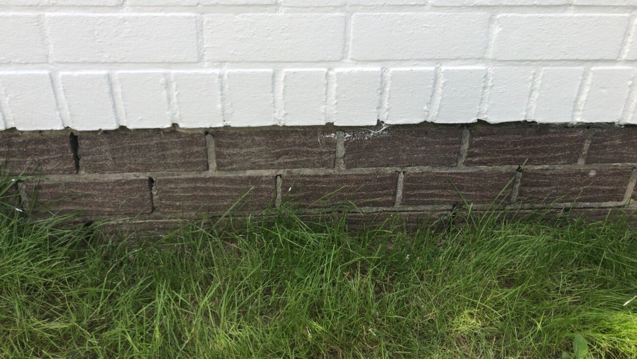 Onderste deel van een witte gevel met stenen en voegwerk.