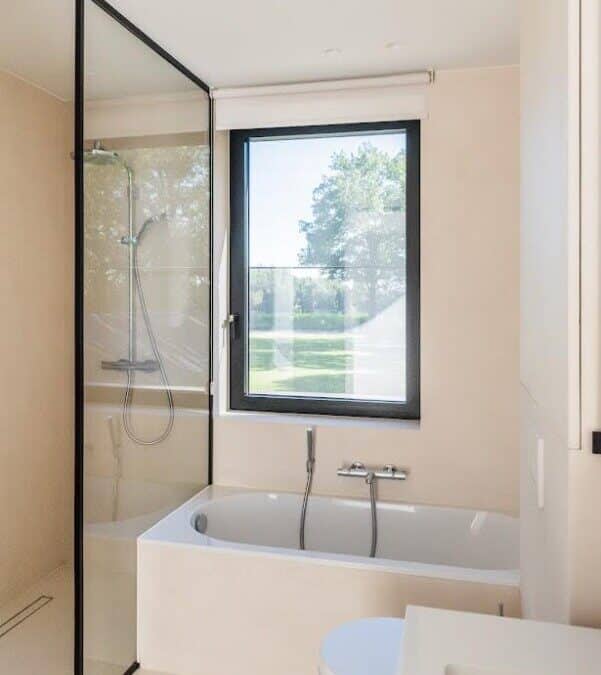 Moderne badkamer met ligbad, glazen douchewand en groot raam in Destelbergen.
