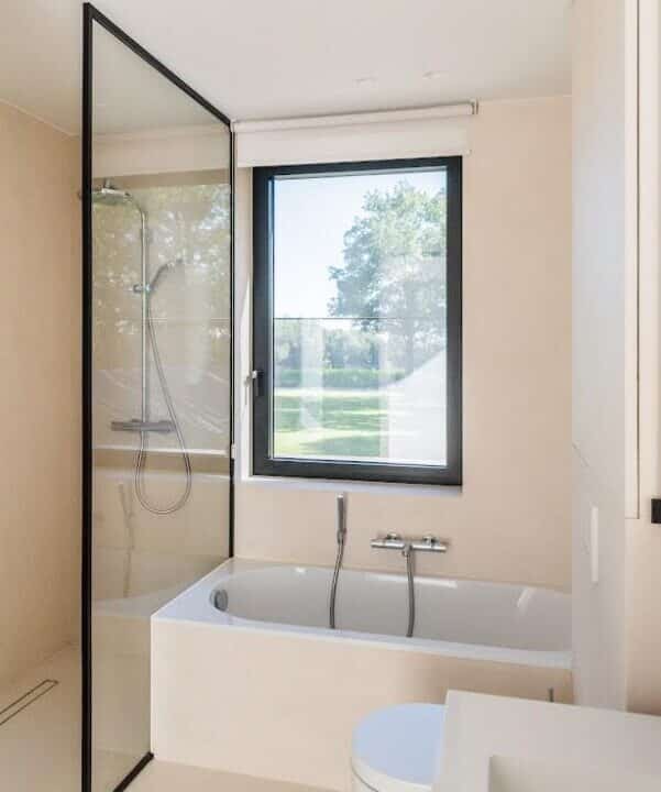 Moderne badkamer met ligbad, glazen douchewand en groot raam in Destelbergen.