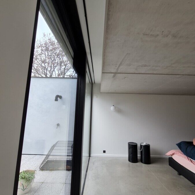 Slaapkamer met glazen schuifdeur en zicht op buitenruimte met muren geverfd aan de hand van een tusk techniek bij een project in Balegem.