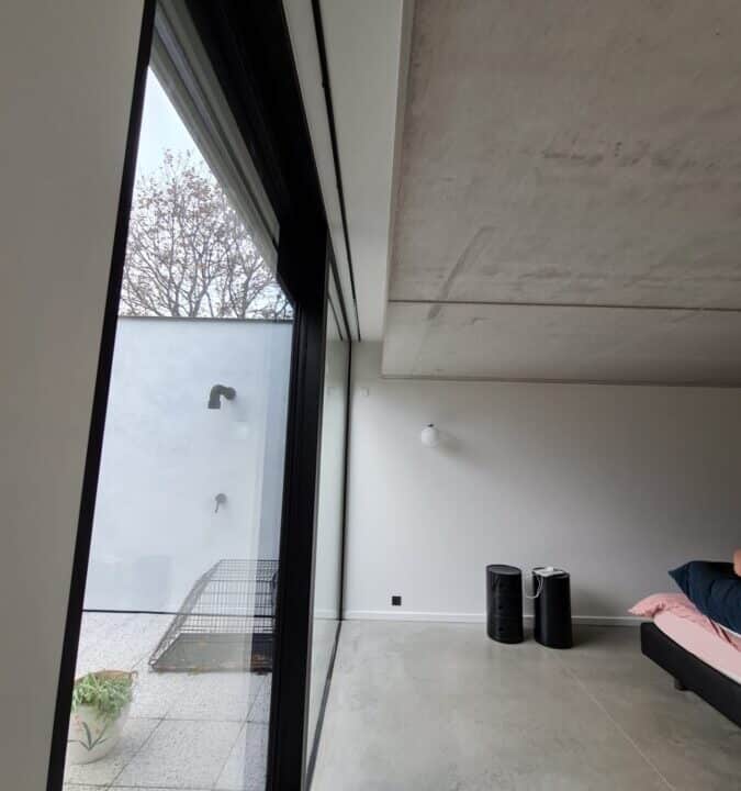 Slaapkamer met glazen schuifdeur en zicht op buitenruimte met muren geverfd aan de hand van een tusk techniek bij een project in Balegem.