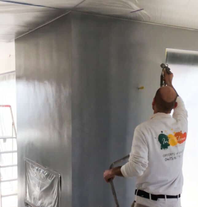 Schilder aan het werk met spuittechniek op een muur, schilderwerken door In't Kleur.