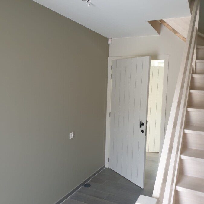 Hal met neutrale muurkleuren en witte binnendeur, onderdeel van een woningproject in Lovendegem.