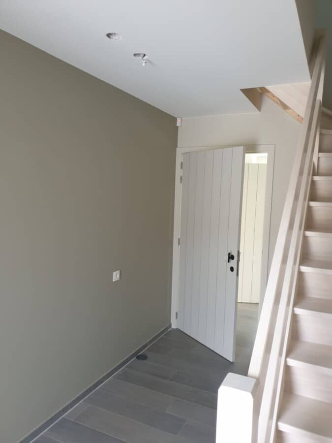 Hal met neutrale muurkleuren en witte binnendeur, onderdeel van een woningproject in Lovendegem.