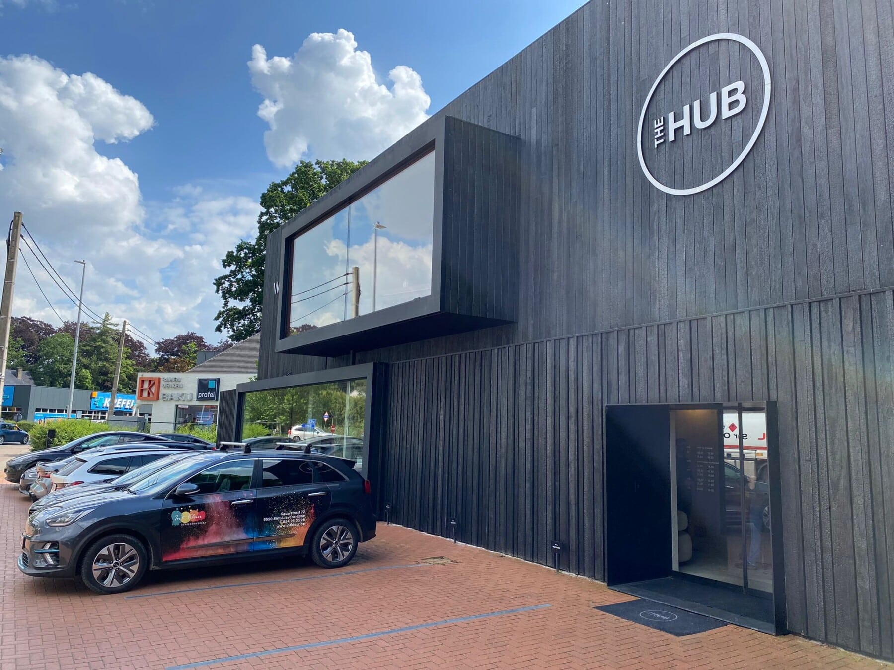 Zwarte gevel van het gebouw The Hub met geparkeerde auto’s op een zonnige dag.