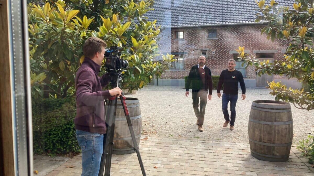 Cameraman filmt twee mannen die buiten lopen richting de ingang van een gebouw.