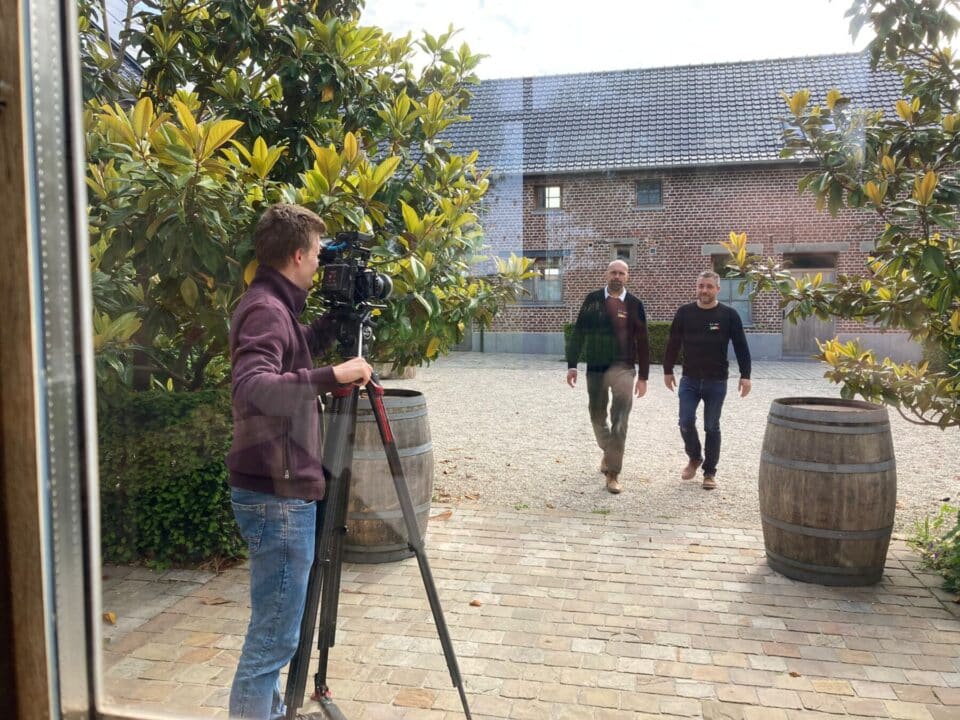 Cameraman filmt twee mannen die buiten lopen richting de ingang van een gebouw.