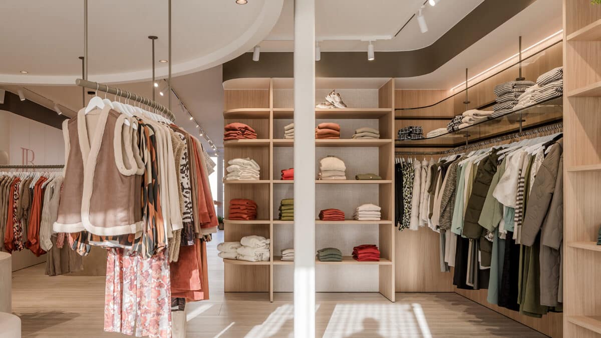 Winkelinterieur met zorgvuldig geplaatste kledingrekken en warme houten accenten, versterkt door de verfijnde schilder- en pleisterwerken van In't Wit en In't Kleur.