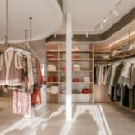 Winkelinterieur met zorgvuldig geplaatste kledingrekken en warme houten accenten, versterkt door de verfijnde schilder- en pleisterwerken van In't Wit en In't Kleur.