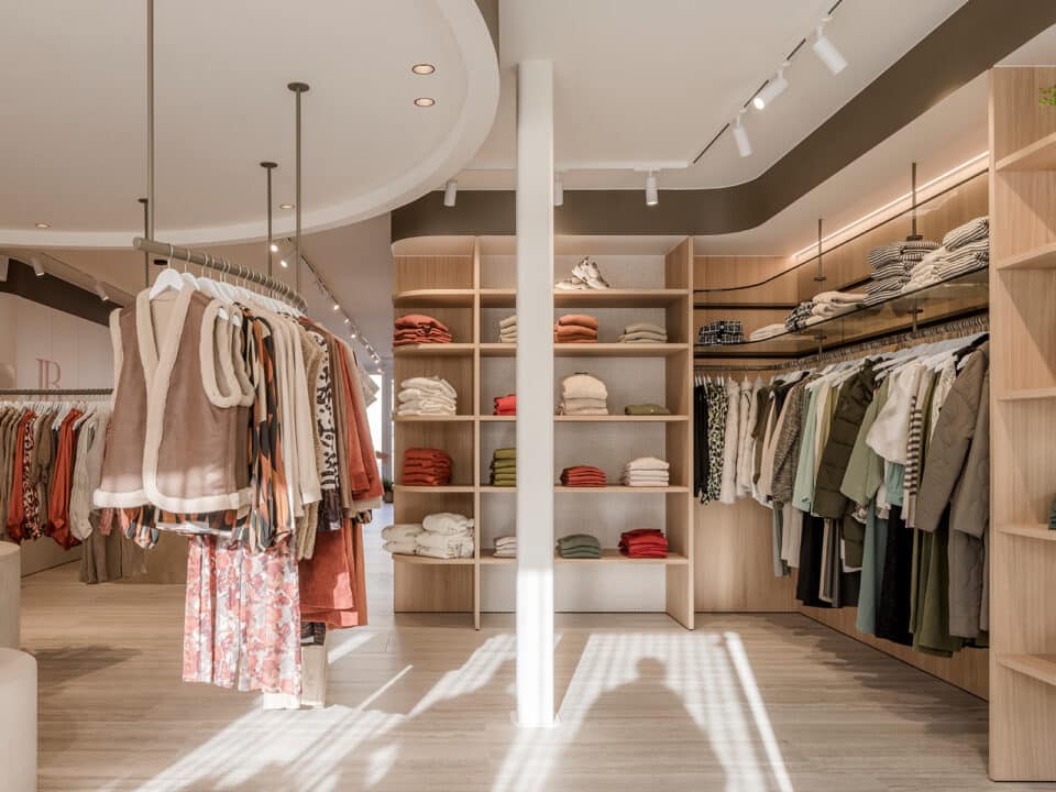 Winkelinterieur met zorgvuldig geplaatste kledingrekken en warme houten accenten, versterkt door de verfijnde schilder- en pleisterwerken van In't Wit en In't Kleur.