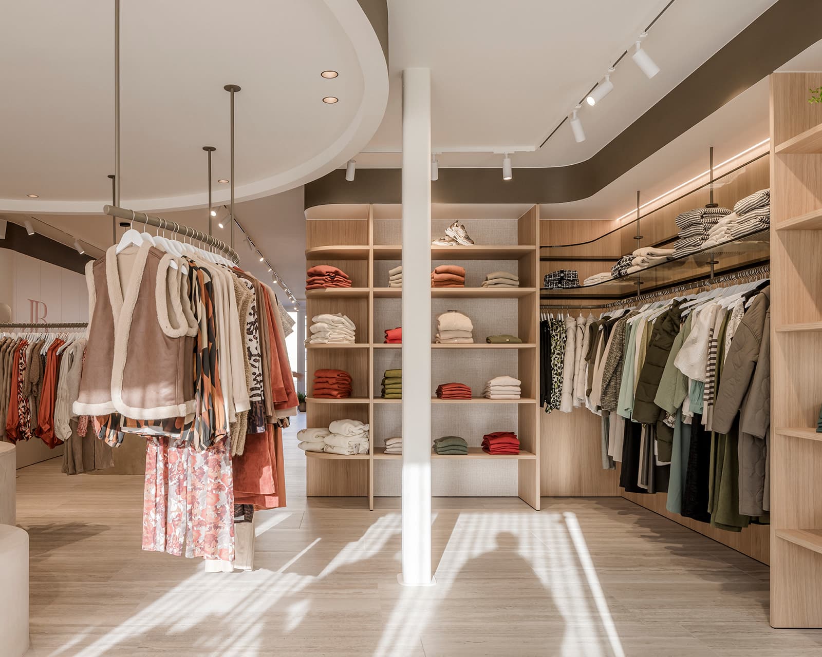 Winkelinterieur met zorgvuldig geplaatste kledingrekken en warme houten accenten, versterkt door de verfijnde schilder- en pleisterwerken van In't Wit en In't Kleur.