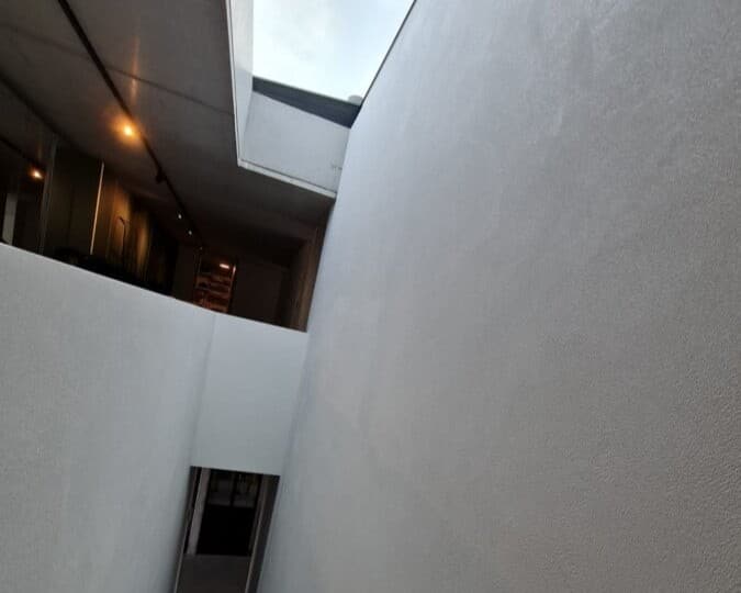 Moderne traphal met witte muren en dakraam - strakke pleisterwerken en schilderwerk door In't Wit en In't Kleur