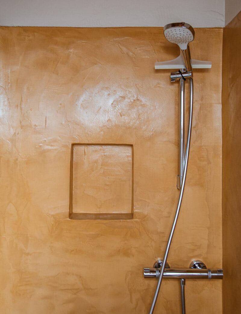 Douchewand met terracotta kleurig decoratief pleisterwerk en ingebouwde nis, afgewerkt met Mortex