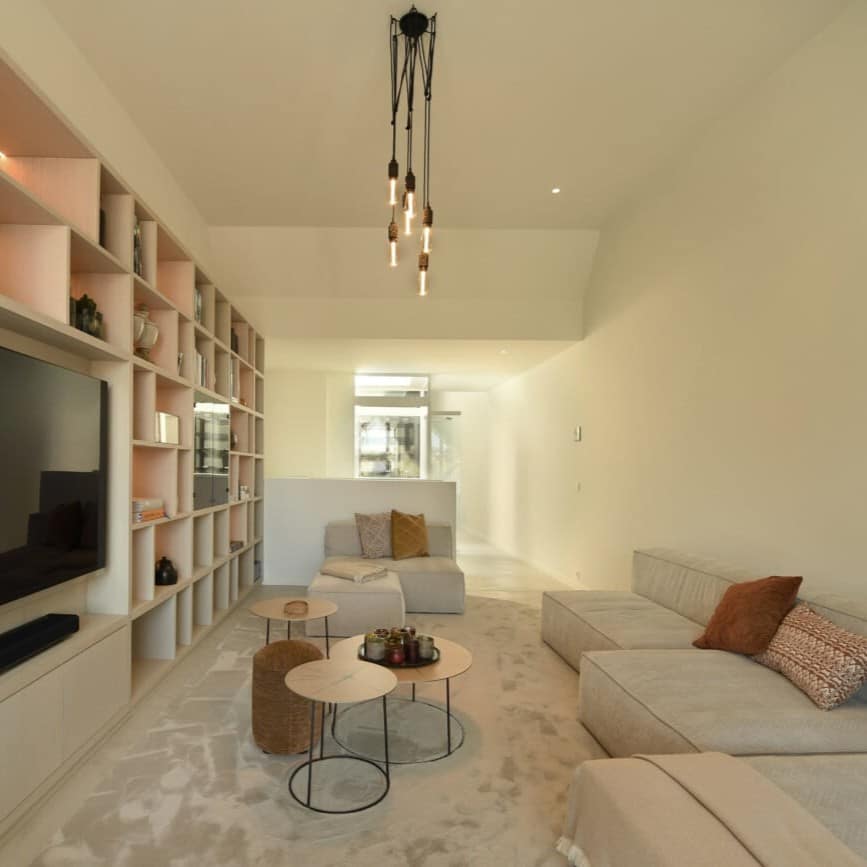Modern wit geschilderd interieur met beige wanden, grijze bank, houten salontafels en ingebouwde boekenkast