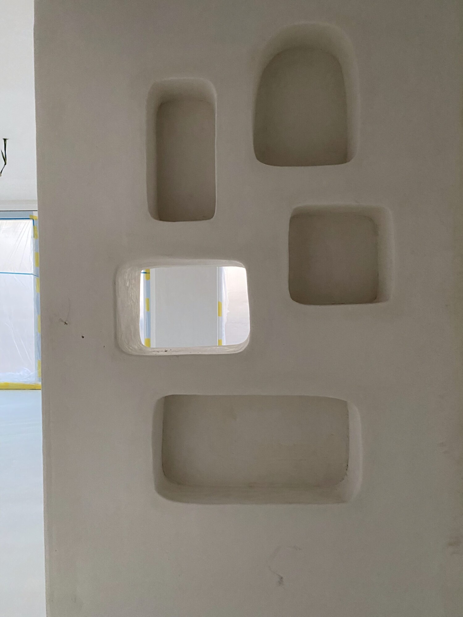 Witte muur met vijf ingebouwde nissen in verschillende vormen - rechthoekig, rond en vierkant - moderne wandafwerking