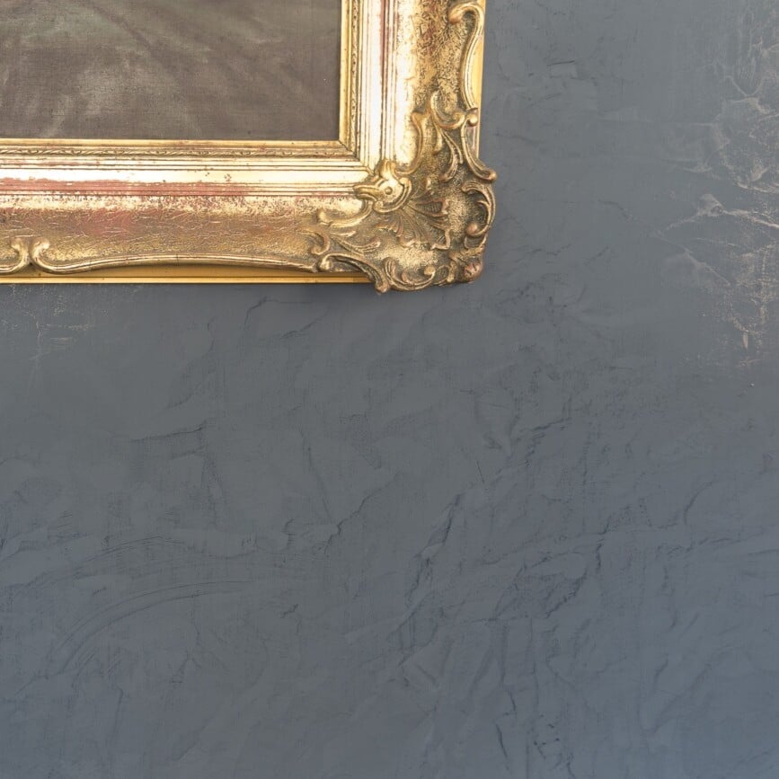 Gouden sierlijst met ornamentele details tegen grijze gestructureerde muur, voorbeeld van decoratieve verftechnieken